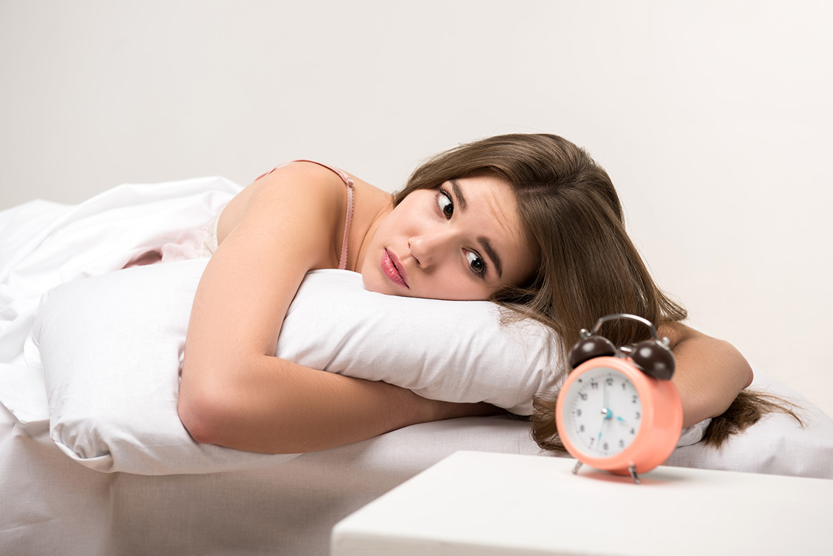 Woman in bed staring at an alarm clock. Sleep deprivation concept.