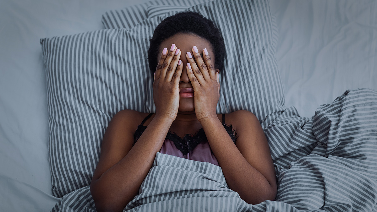 Woman lies on striped bedding with hands over face, trying to sleep.